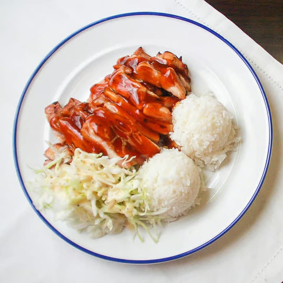 Teriyaki chicken with white rice and coleslaw on a white plate with a blue rim.