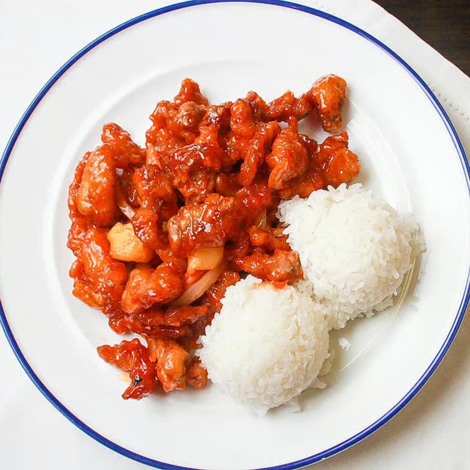 Sweet and sour chicken with pineapple and onions, served with two scoops of white rice.