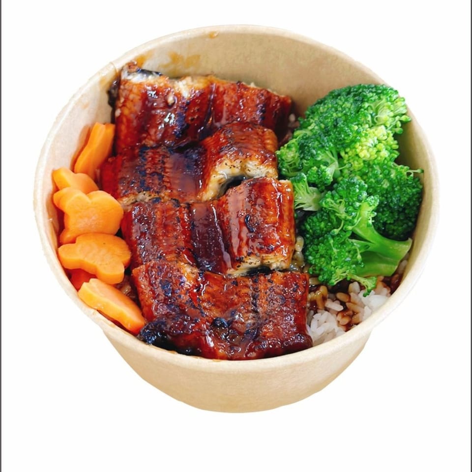 Unagi donburi with grilled eel, white rice, broccoli, and star-shaped carrots in a paper bowl.