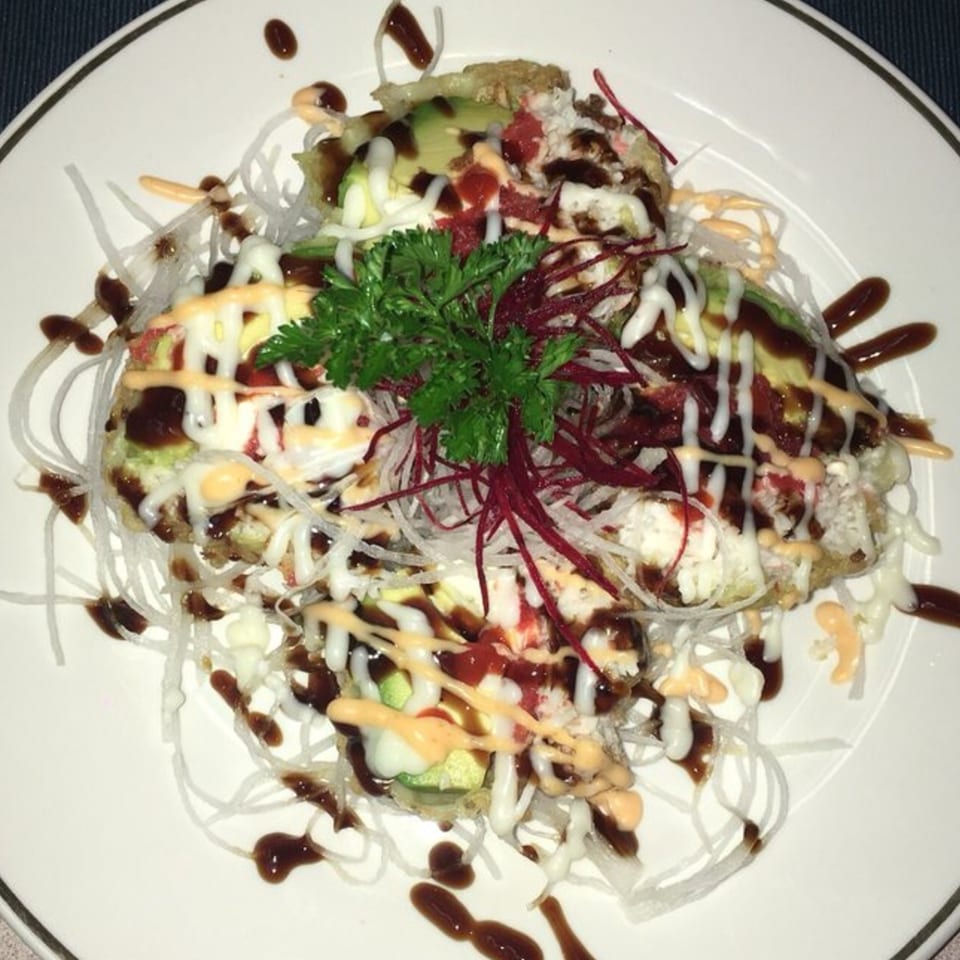 Sake Sushi + Grill's Japanese dish, topped with avocado, sauces, and fresh herbs on a white plate.