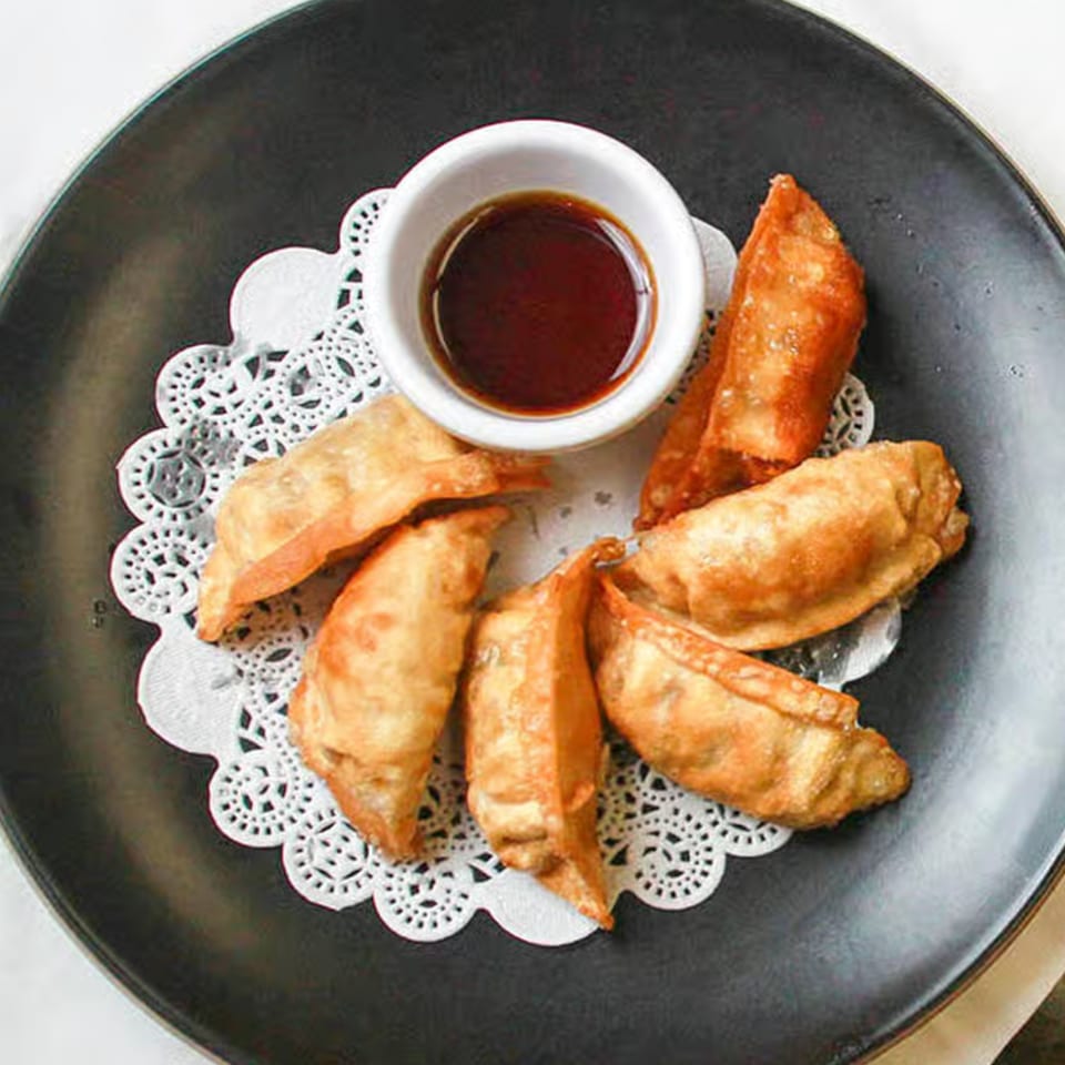 Golden-brown fried gyoza dumplings with a side of dark dipping sauce on a black plate.