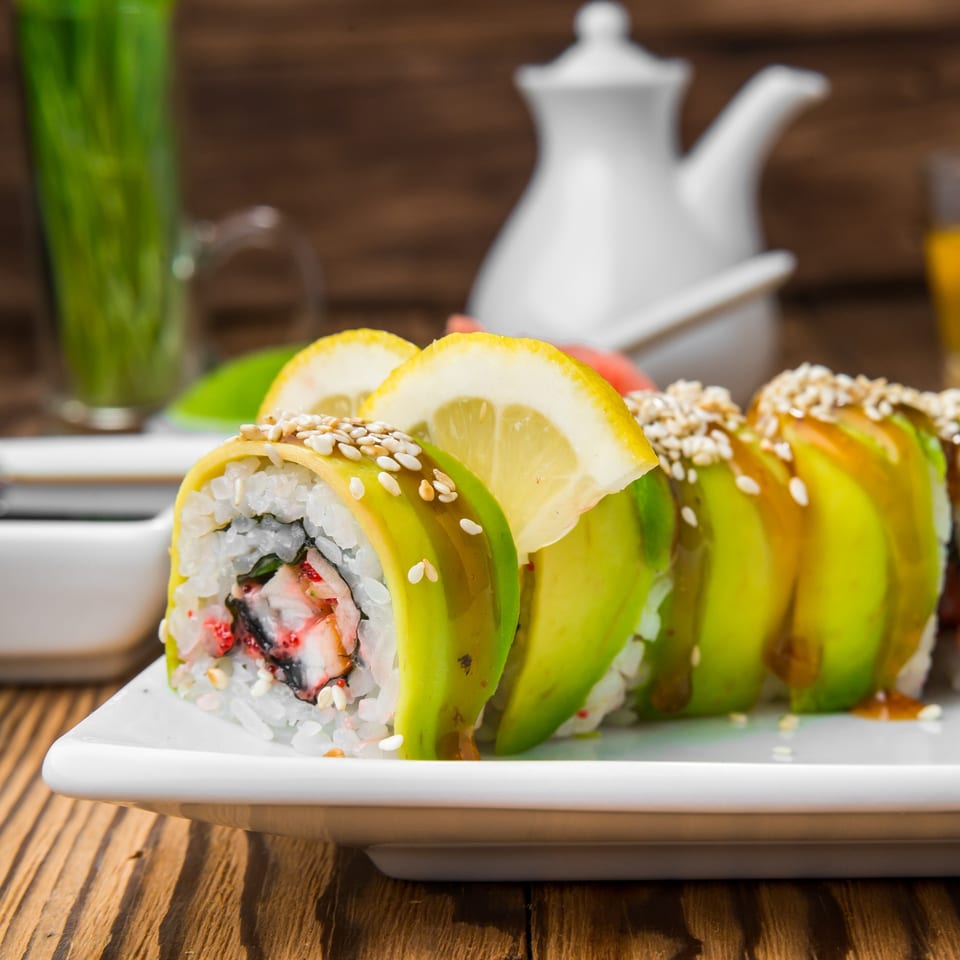 Sake Sushi + Grill's avocado sushi rolls with sesame seeds and lemon slices on a white plate.
