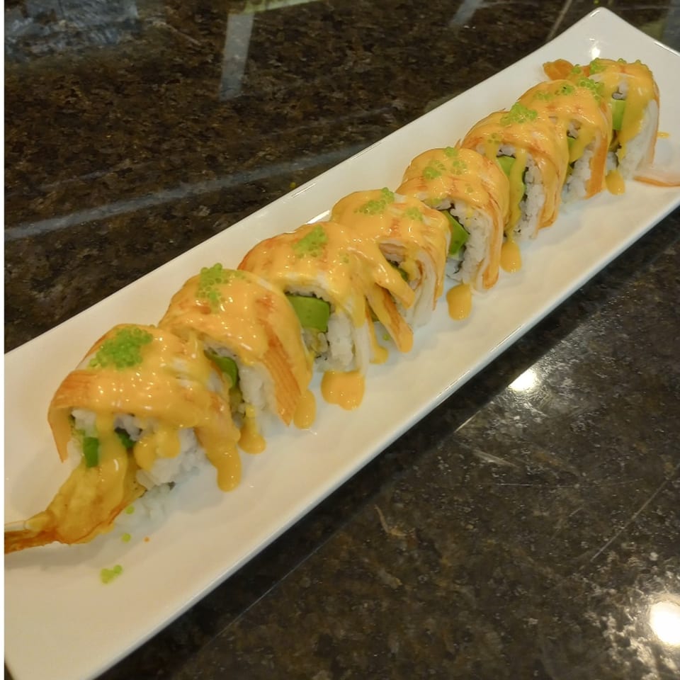 A long white plate holds eight pieces of Sake Sushi + Grill's sushi rolls, drizzled with orange sauce.